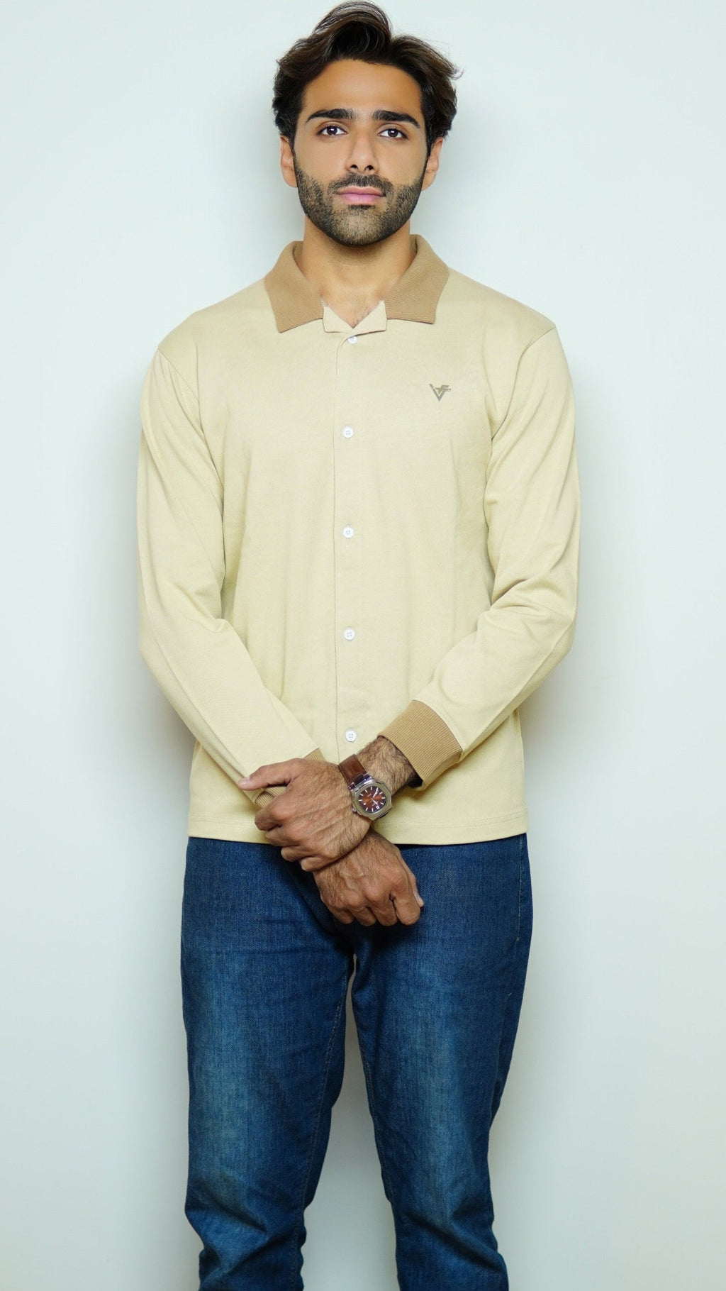 Man wearing a light-colored sweater with a collar and blue jeans against a white background