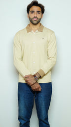 Man wearing a light-colored sweater with a collar and blue jeans against a white background