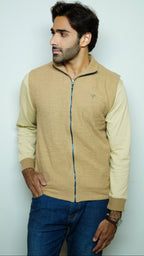 Man wearing a beige zip-up jacket and blue jeans against a light gray background