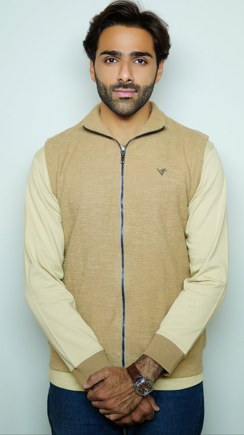 Man wearing a beige vest over a cream shirt with a light gray background