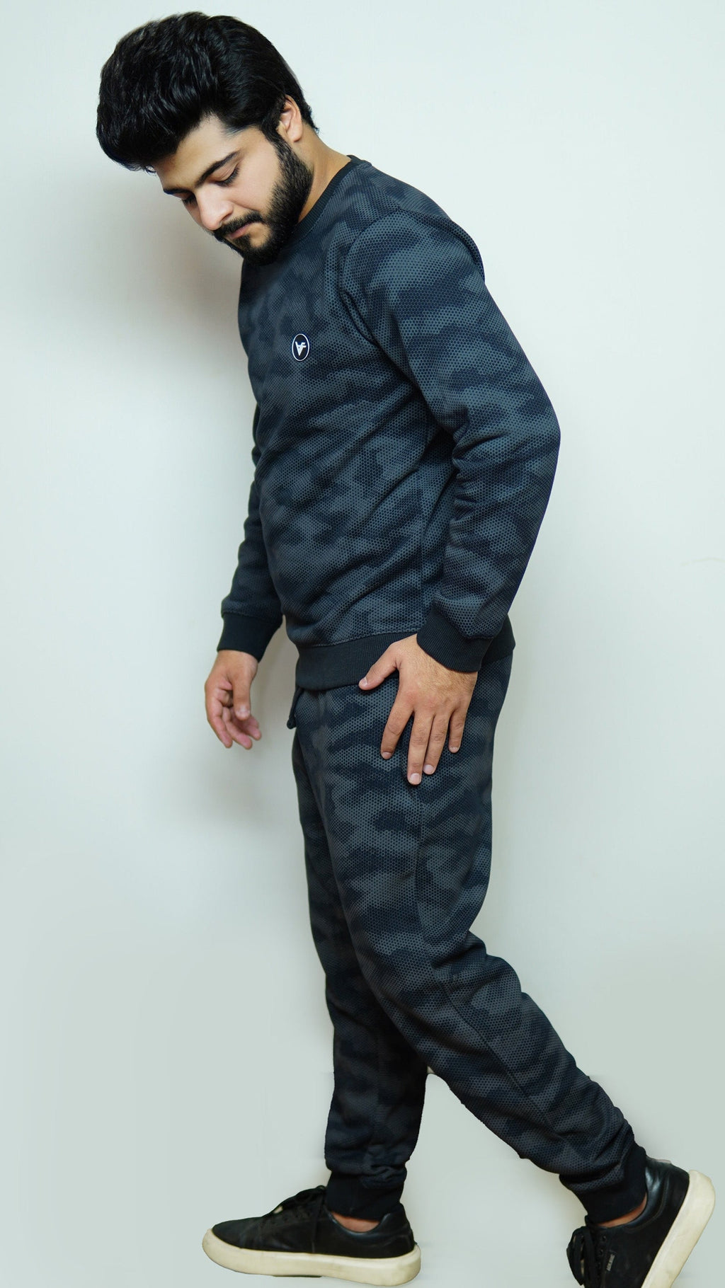 Man wearing a dark camouflage tracksuit against a white background