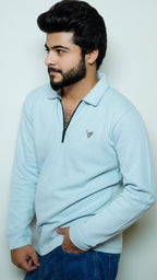 Man wearing a light blue sweater with a small logo on a plain background