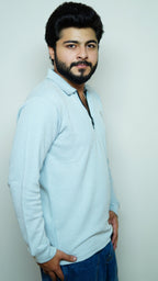 Man wearing a light blue sweater and dark pants against a plain background